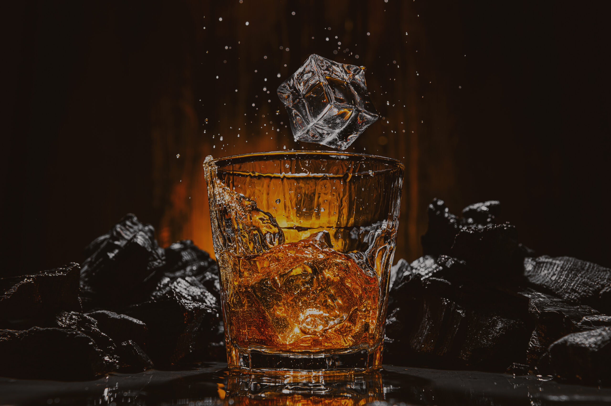 ice cubes fall into a glass with a brown alcoholic drink Whiskey in a glass